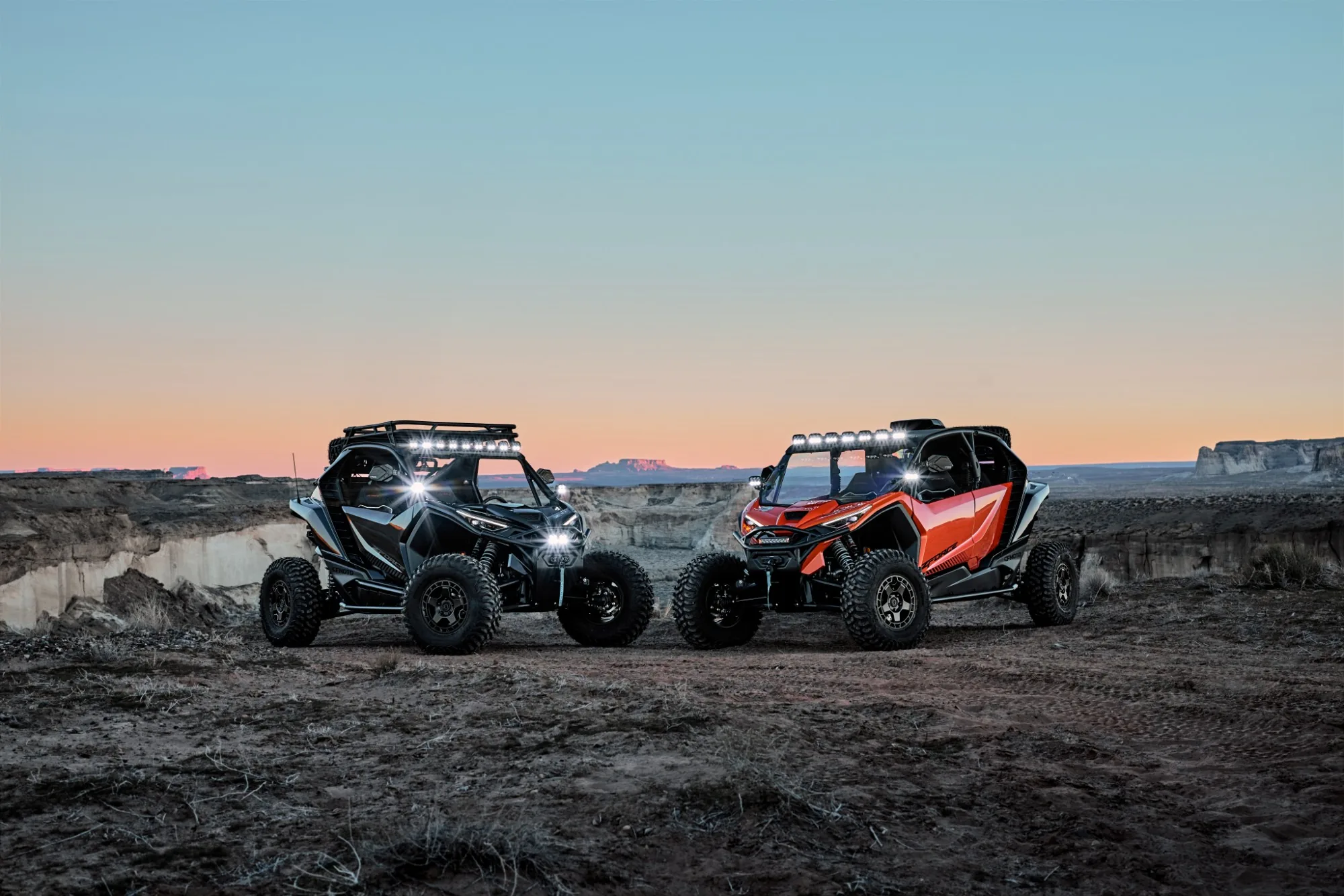 Dos CFMOTO ZFORCE con barras de luces LED encendidas al atardecer, frente a frente en el desierto